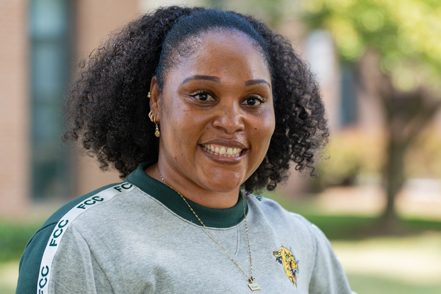 A smiling woman with curly hair wearing a grey and green FCC sweatshirt outdoors.
